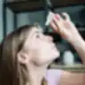 Moteris į akis lašinasi akių lašus